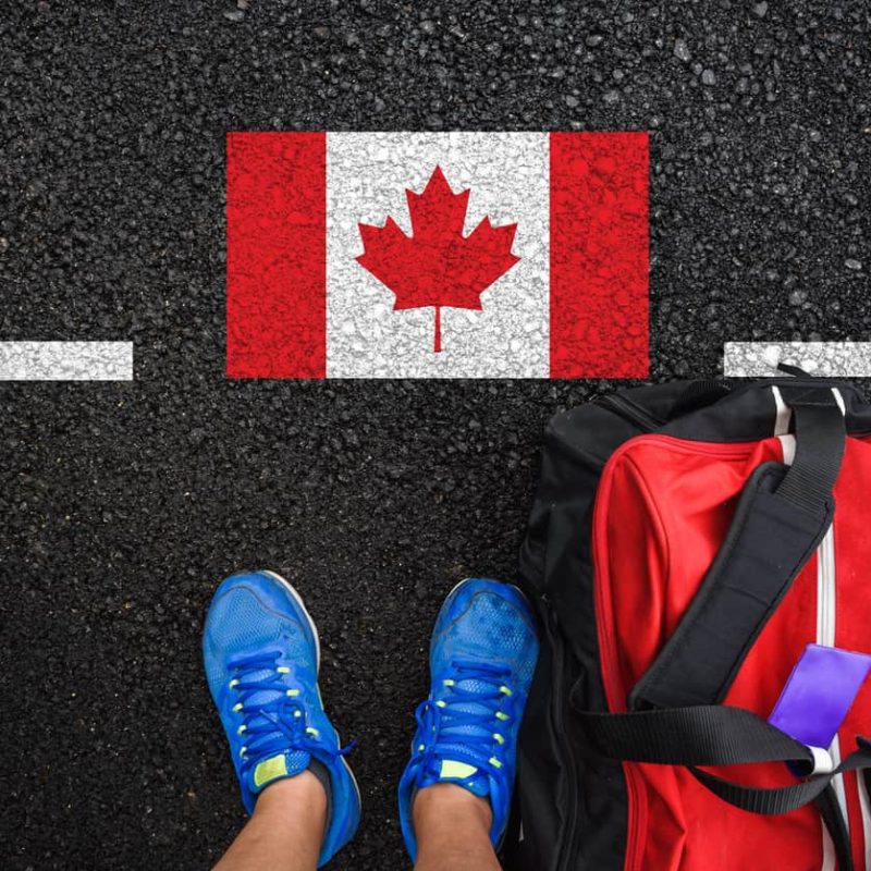 a man with a shoes and travel bag is standing on asphalt next to flag of Canada and border